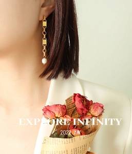Detail of long gold chain earrings with a freshwater pearl on a model in beige suit