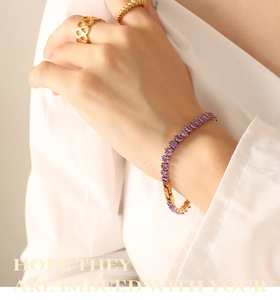 Detail of purple oval gemstone bracelet with gold rings on a white shirt background