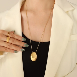Collier à pendentif ovale doré et bagues texturées sur mannequin en costume blanc élégant