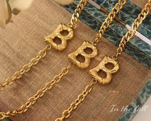 Detailed close-up of golden B-letter pendant with bamboo texture on thick chain