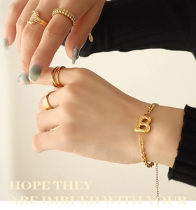 Detail of gold Cuban chain bracelet with B-letter pendant and stacked rings on a model