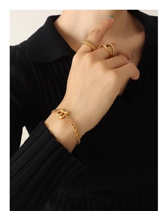 Close-up of gold chunky Cuban chain bracelet with letter B pendant and rings on model