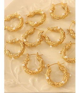 Detail of gold U-shaped earrings with hammered texture, pearls and sparkling zircons