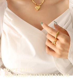 Primo piano di una collana con ciondolo a cuore dorato e anelli indossati da una modella
