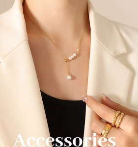 Close-up of elegant gold pearl necklace and textured rings worn with a blazer