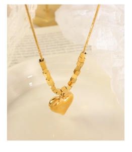 Primo piano della collana con ciondolo a cuore dorato e perle quadrate su vassoio