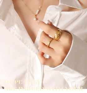 Close-up of elegant gold pearl necklace and gold rings set on minimalist white shirt
