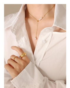 Close-up of elegant gold Y-necklace with pearls and polished gold rings on white fabric