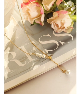 Detail of elegant gold-toned pearl necklace with layered pendants on a floral backdrop