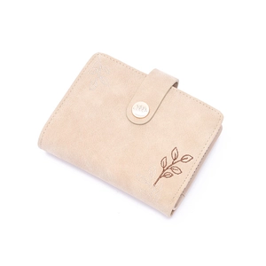 Macro detail of leaf embroidery and metallic snap closure on beige leather wallet