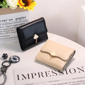 Close-up of beige and black bi-fold wallets with cloud-shaped metal clasps on white table