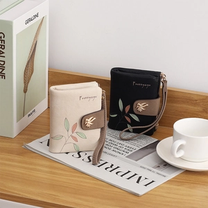 Detail of short PU leather wallets with leaf print and metal bird clasp on a wooden desk