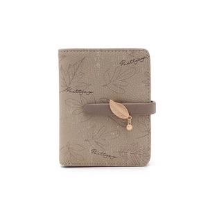 Close-up of brown leather wallet with leaf print, brand logo and metal leaf pendant
