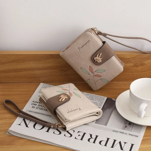 Detail of the chic floral bifold wallet featuring leaf-shaped gold buckle and wrist strap