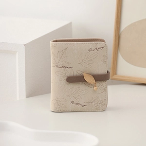 Close-up of beige leaf-printed wallet with gold leaf pendant and button closure