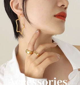 Detail view of model wearing gold hollow star earrings and chunky polished metal rings