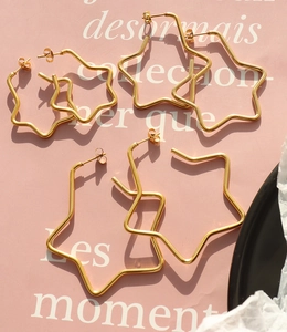 Three pairs of golden star hoop earrings in varying sizes on a chic pink background
