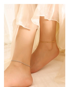 Close-up of minimalist gold and silver anklets worn by a model on light fabric