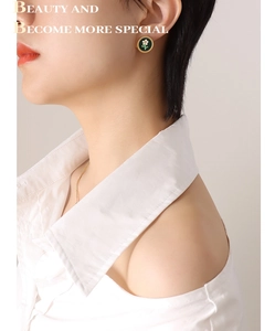 Detail of round gold stud earring with green enamel and white flower on model