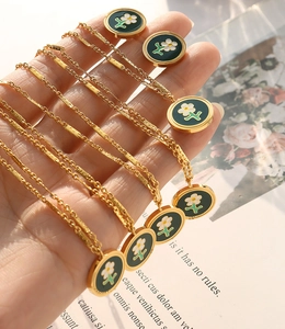 Close-up of gold chain necklaces with green enamel daisy pendants held in hand