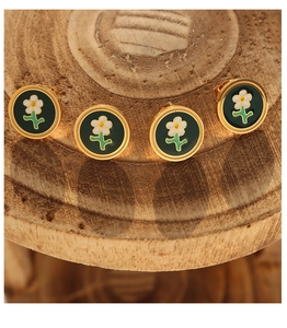 Detail view of round gold-trimmed floral stud earrings with green enamel on a wooden base