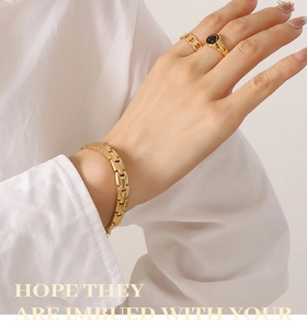 Detail von goldenem Armband und Siegelring mit Smiley auf der Hand eines Models