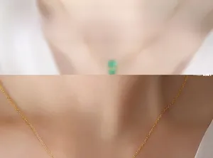 Détail macro de la fine chaîne dorée et du pendentif serti d'une pierre verte