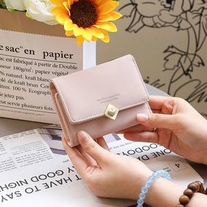 Vue détaillée du portefeuille rose pâle pour femme avec fermoir cœur doré tenu à la main
