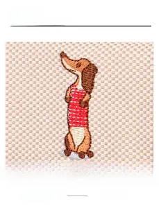 Détail de broderie teckel sur toile beige à carreaux avec garniture en cuir rouge