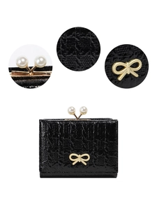 Detail view of black patent leather wallet with pearl clasp and gold bow decoration