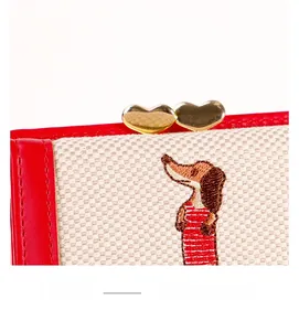 Détail de la broderie et du fermoir cœur doré sur un portefeuille pliable