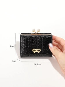 Close-up of black patent leather trifold wallet with golden bow and pearl buckle details