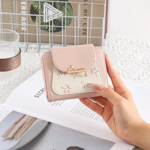 Pink floral bifold wallet with gold leaf charm held in a lifestyle setting