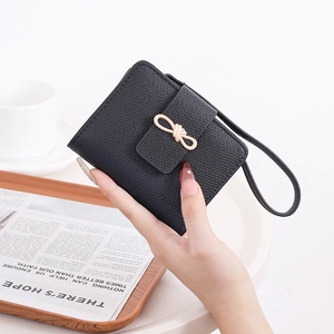 Close-up of black lychee grain wallet featuring a gold bow clasp and hand strap