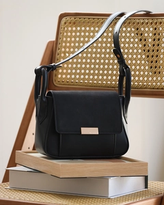 Close-up of black crossbody bag with gold metal buckle on a minimalist wooden decor