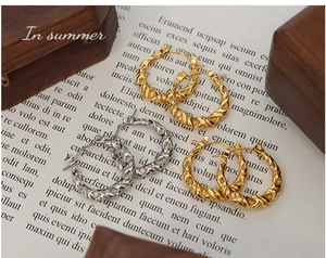 Détail de boucles d'oreilles créoles torsadées or et argent sur fond de papier vintage