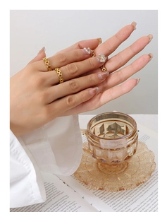 Detail of gold chain link rings and a zircon bow ring worn by a model on a desk