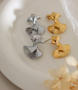 Detail of vintage textured fan-shaped earrings in gold and silver on white ceramic plate