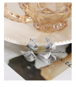 Detail shot of silver fan-shaped earrings with hammered texture on a ceramic plate