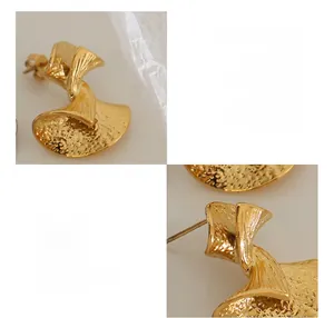 Close-up of golden fan-shaped earrings with textured surface and metallic luster
