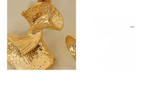 Macro detail showing gold扇形 earrings with hammer-textured finish and abstract style