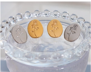 Detailed close-up of oval titanium earrings with embossed rose pattern in gold and silver