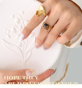 Detail of lava style gold ring and tiger eye stone ring on hand over white porcelain