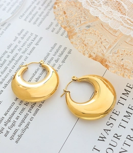 Detailed view of chunky 18K gold plated titanium hoop earrings on a vintage prop background