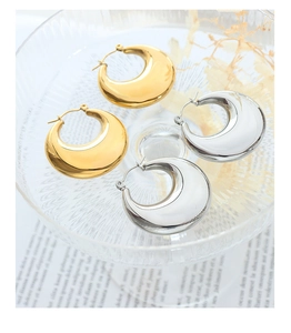 Detailed view of thick gold and silver polished hoop earrings on a textured glass tray