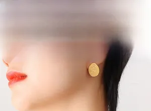 Close-up of model wearing gold oval titanium steel earrings with embossed rose detail