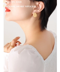 Detailed view of golden oval earrings with rose relief engraving worn by a model