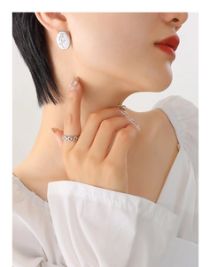 Close-up of model wearing oval rose embossed earrings and cuban chain style ring