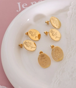 Close-up of golden oval stud earrings with embossed rose patterns on white lace
