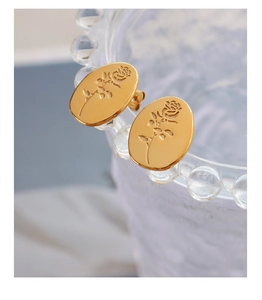 Macro shot of gold oval titanium steel earrings with embossed rose flower design details